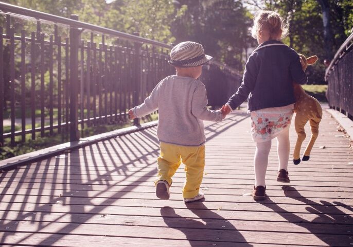 Two children holding hands walking across a bridge